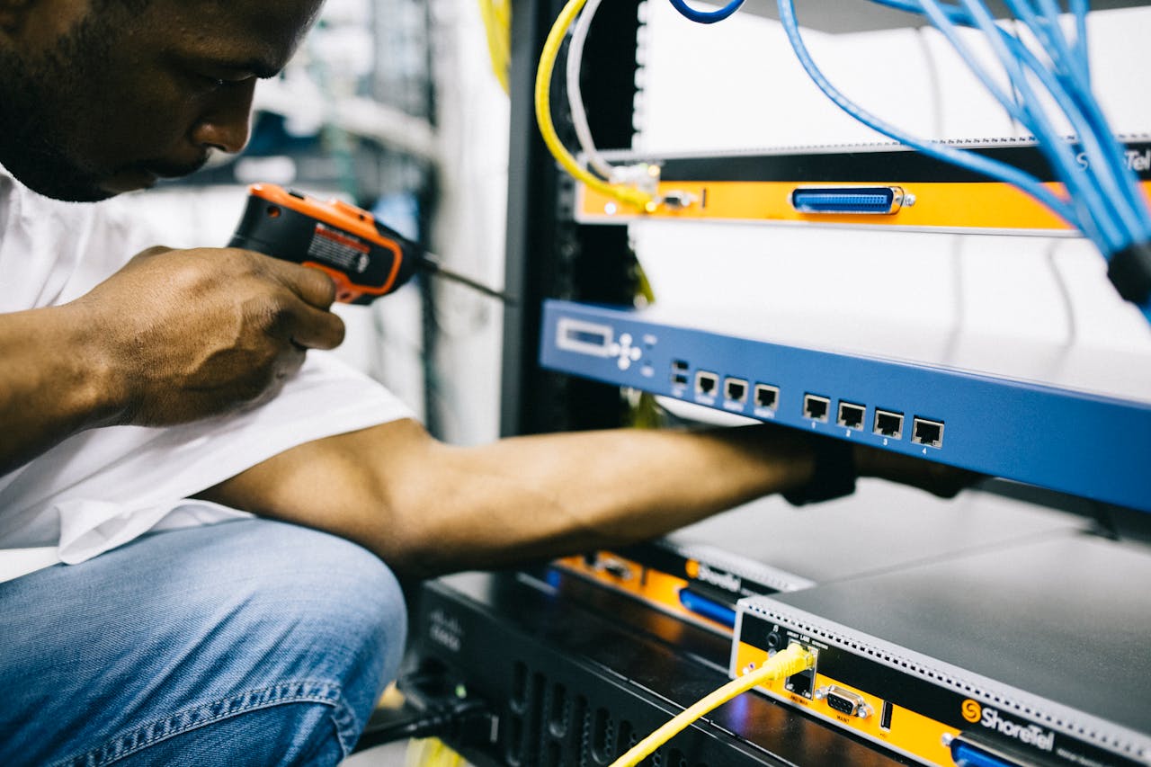 Home Side view crop concentrate African American male mechanic in jeans and white shirt using screw gun while working with hardware